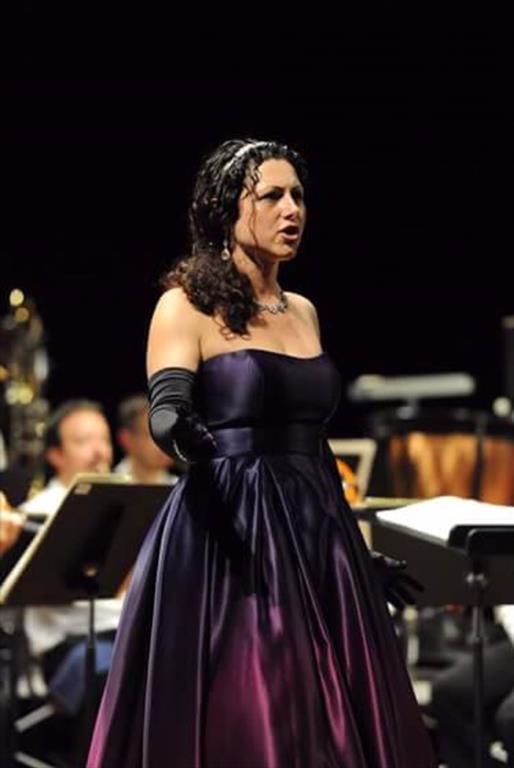 Female opera singer in purplse dress standing alone singing on a stage 